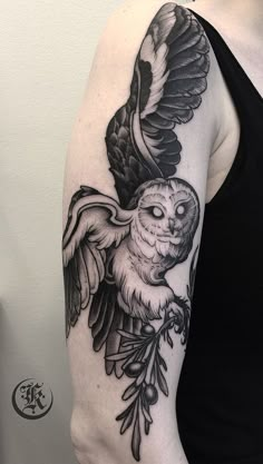 a black and white owl tattoo on the right arm, with an olive branch around it