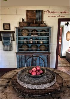 an old fashioned wooden table with apples in a bowl on top of it, next to a blue hutch