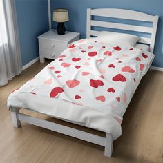 a white bed with hearts on it in a blue room next to a nightstand and window