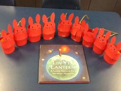 a bunch of little red paper rabbits sitting on top of a table next to a book