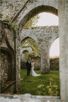 a bride and groom standing in an old stone archway at the end of their wedding day