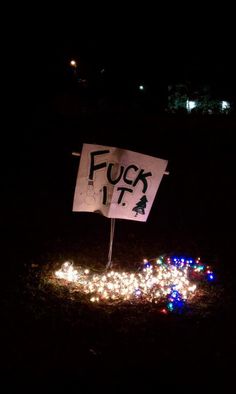 a sign that is sitting in the grass with christmas lights around it and some trees