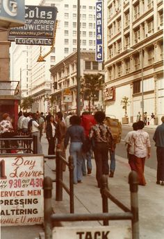 many people are walking on the sidewalk near buildings