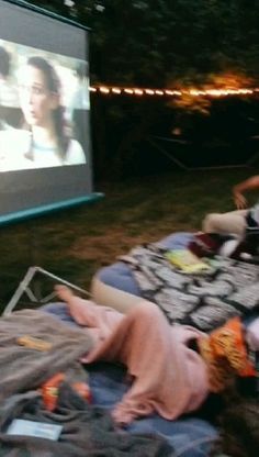 people sitting in the grass watching movies on a big screen at an outdoor movie theater