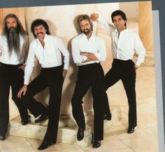 three men with long hair and beards are posing for a photo in front of a wall