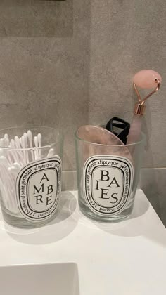 two glass cups with toothbrushes in them on a counter