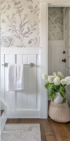 a white bathroom with floral wallpaper on the walls and wood flooring in front of it