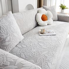 a white couch with pillows on top of it and a cup in front of it