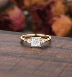 a gold ring with a princess cut diamond in the center on top of a wooden table