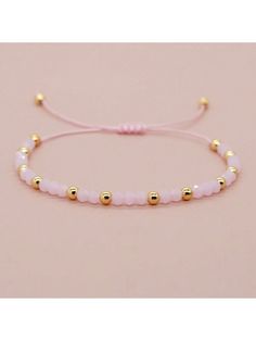 a pink beaded bracelet with gold beads on a light pink background and a white cord