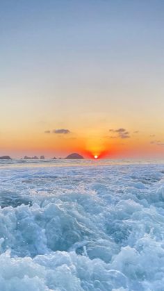 the sun is setting over the ocean with waves in the foreground and an island in the distance