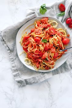 a white plate topped with pasta covered in tomato sauce and garnished with basil