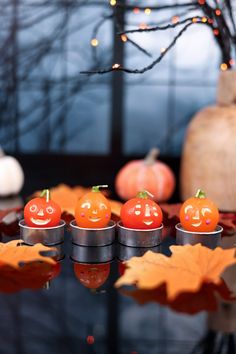 small pumpkins with faces on them sitting in front of some autumn leaves and a tree