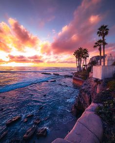 the sun is setting over the ocean with palm trees