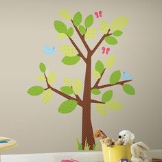 a child's room with a tree painted on the wall and stuffed animals nearby