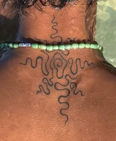 the back of a woman's neck with a tattoo on her left side and green beads