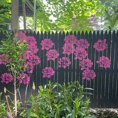 a black fence with pink flowers painted on it and green plants in the foreground