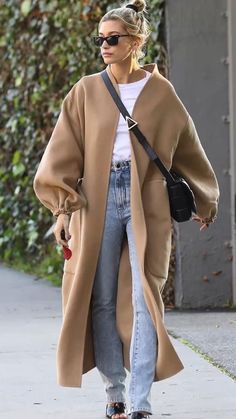 a woman walking down a sidewalk while wearing jeans and a long cardigan coat with an open front