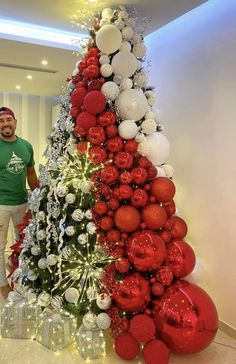 a man standing next to a christmas tree with red and white ornaments on it's sides