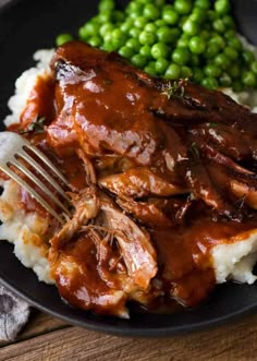 a black plate topped with meat and mashed potatoes next to green pea sprouts