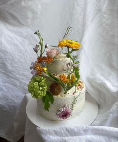 a three tiered cake with flowers and leaves on the top is sitting on a white plate