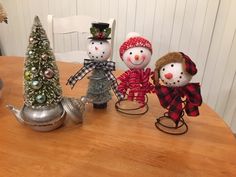 three snowmen sitting on top of a wooden table next to a teapot and christmas tree