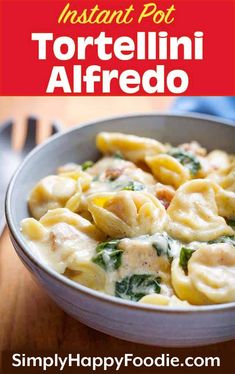 a white bowl filled with tortellini alfredo and spinach on top of a wooden table