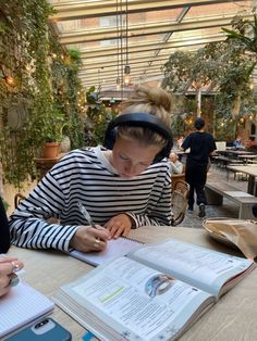 a woman sitting at a table writing in an open book with headphones on her ears