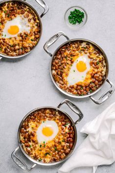 three pans filled with eggs and beans on top of a white table next to a napkin