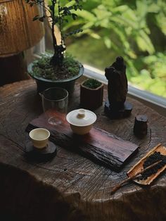 a wooden table topped with cups and saucers next to a potted plant on top of a window sill