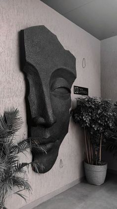 a plant in a pot next to a wall with a face on it