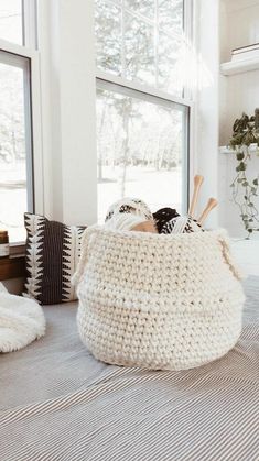 a large white basket sitting on top of a bed next to a window filled with plants