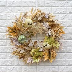 a wreath is hanging on the wall with leaves and pumpkins in front of it