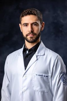 a man wearing a white lab coat and black tie posing for a photo in front of a dark background