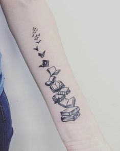 a person with a tattoo on their arm that has books coming out of them and flying up into the air