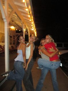 three women posing for the camera with their arms around each other on a sidewalk at night