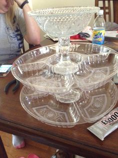 a woman sitting at a table with a glass cake dish on it's side