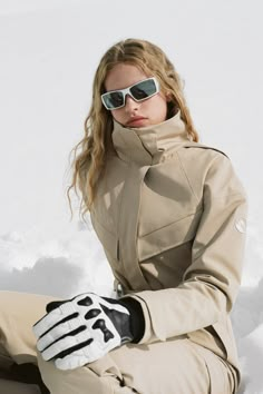 a woman sitting in the snow with her hands on her knees wearing sunglasses and gloves