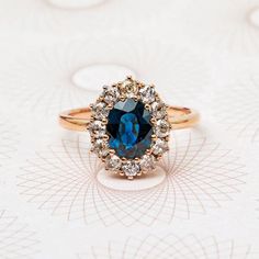 a ring with a blue stone surrounded by white and brown diamonds on a floral background