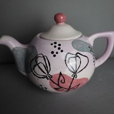 a teapot with flowers painted on it sitting on a counter top next to a wall