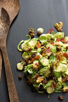 a salad with bacon, lettuce and walnuts on a black surface next to a wooden spoon