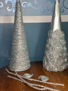 two silver christmas trees sitting on top of a wooden table next to a blue wall