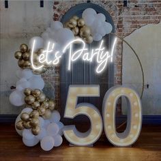 the 50th birthday sign is lit up with white and gold balloons, which spell out let's party 50