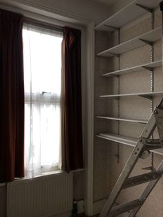 an empty room with some shelves and a ladder in the corner next to a window