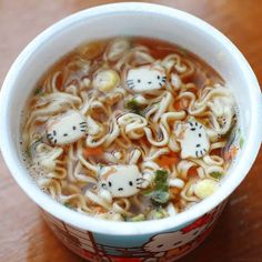 a cup of soup with noodles and cats on the top, in front of a woman's face