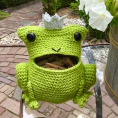 a crocheted frog sitting on top of a table next to a flower pot