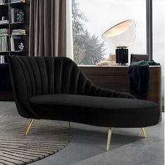 a black couch sitting in front of a window next to a book shelf and lamp