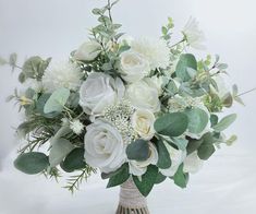 a vase filled with white flowers and greenery