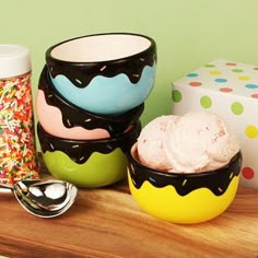 three bowls with ice cream and sprinkles sit on a table next to two cups