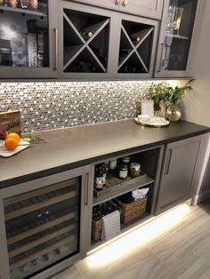 a kitchen with grey cabinets and white tile backsplashing, wine bottles on the counter